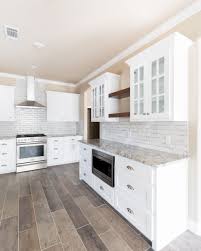 White Kitchen With Stained Floating Shelves Wood Look Tile Floor And Stainless Range Hood Kitchen Backsplash Designs Kitchen Floor Tile Wood Look Tile Floor