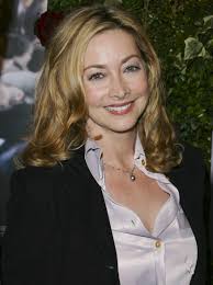 Sharon Lawrence with long hair, curls, and wearing a shiny silk shirt
