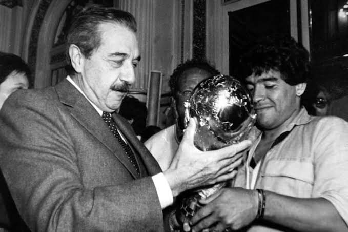 Diego Maradona y Raúl Alfonsín sostienen la Copa del Mundo en la Casa Rosada., generada por IA