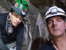 Aerial view of the Burns-Moore mine complex including the tunnel and  powerhouse. A small group of miners pose outside the tunnel portal with a  filled mine cart.