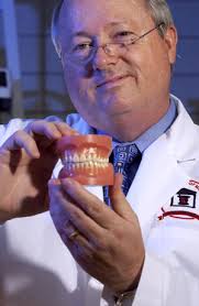 Michael A. Repka displays a transmucosal patch, placed just above the gumline (top center) of this set of false teeth. UM photo by Robert Jordan. - Repka2