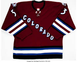 A white with sliver trim triangle with the letter c in maroon with white trim on a dark blue mountain background. 2003 04 Derek Morris Game Worn Colorado Avalanche Jersey Rare Lot 82232 Heritage Auctions