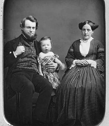 In 1873, a family is shown carefully posed for a photographic portrait,  reflecting the formal conventions of early photography. Long exposure times  required subjects to remain still, resulting in composed expressions and