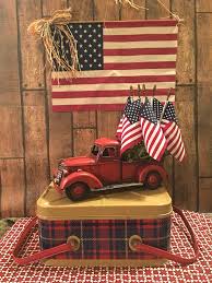 This magnificent tiered tray decoration with some patriotic day colors, flags, mason jars, and lilies looks adorable. Simple But Very Patriotic With Vintage 1950 S Nesco Tartan Plaid Picnic Basket And Red Toy Truck A 4th Of July Decorations Red Truck Decor Fourth Of July Decor