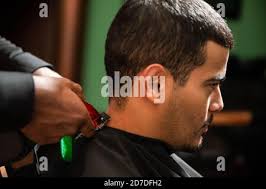 Un barbiere afroamericano taglia e rasa i capelli di un uomo latino  ispanico con un pizzetto e baffi con un rasoio elettrico in un barbiere  Foto stock