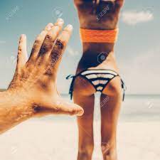 Mans Hand Trying To Touch Tanned Fit Butt Of A Sporty Young Beautiful  Female In A Sexy Stripped Bikini On A Sea Shore Background. Outdoor  Lifestyle Picture On A Hot Sunny Summer