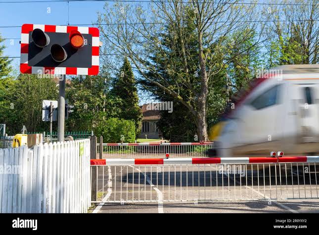 Railway level crossing with gates down in rural area. Church Lane, Margaretting, Essex, leading to church. Warning light. Train passing at speed Stock Photo - Alamy