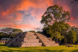 Ancient Mayan temple ruins at Copán with detailed stone carvings and hieroglyphs illuminated by dramatic sunset lighting