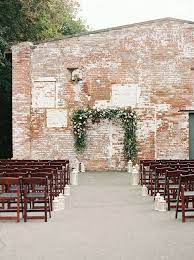 Industrial Wedding Ceremony Decor Idea Exposed Brick Backdrop With Greenery Arch Industrial Wedding Ceremony Industrial Wedding Wedding Ceremony Decorations