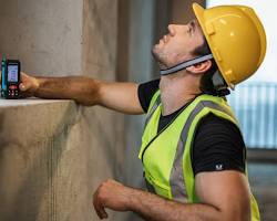 Image of surveyor using a laser distance meter to measure a building