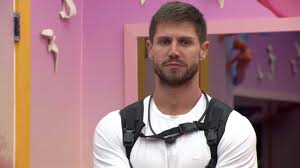 Arthur Aguiar, participante do BBB 22, em um momento sério dentro da casa. Ele usa uma camiseta branca e um acessório nas co…