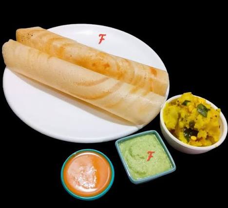 Close-up of crispy dosa batter being spread thinly on a hot cast-iron griddle with steam rising