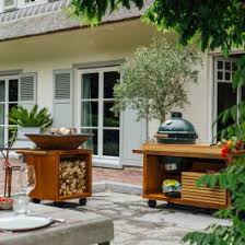 The outdoor kitchen design selects the big green egg beside the stove that lies next to the sink unit. Ofyr Kamado Table Corten 135 Pro Teak Wood Bge