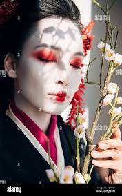 beautiful geisha with red and white makeup and sakura in sunlight Stock  Photo - Alamy