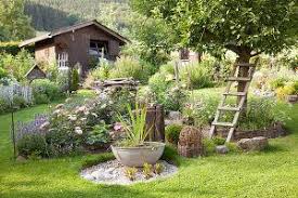 Landlicher Garten Mit Bluhenden Beetinseln Schale Mit Wasserpflanzen Auf Gekiester Flache Im Hintergrund Gartenhaus Garten Abschussiger Garten Cottage Garten