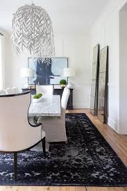 This dining room features a beige area rug with black writing and a light wood dining table paired with high back chairs. Marble Dining Table On Black Faded Rug Transitional Dining Room