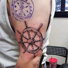 This compass tattoo appears to be a tribute to a sailor of some sort, as it features a ship's wheel and an anchor. 3d Ship Wheel Nautical Upper Arm Tattoos For Men Nautical Tattoo Helm Tattoo Tattoos For Guys