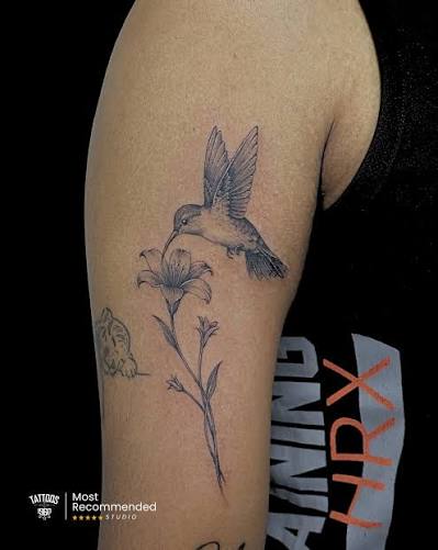 Fine Line Hummingbird Tattoo by Tattoos1960 Pune Delicate fine line realism executed with controlled black and grey tonal layering, precision feather detailing, and balanced contrast mapping. This hummingbird and floral composition was