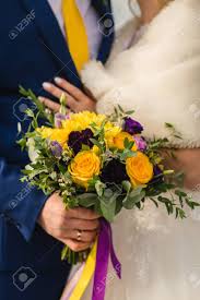 Wedding registry, honeymoon fund, cash fund Bridal Bouquet On The Wedding Day A Lovely Girl Holds A Bouquet Of Yellow Roses And Purple Flowers The Groom In A Blue Suit Hugs The Waist Of The Bride Stock Photo