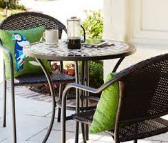 A Patio Bistro Set With A Table Two Chairs And Green Pillows Patio Furniture Table Wrought Iron Patio Furniture Wicker Patio Chairs