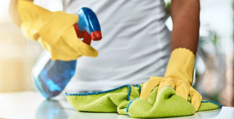 Professional housekeeper using a high-efficiency vacuum on a hardwood floor in a sunlit living room.