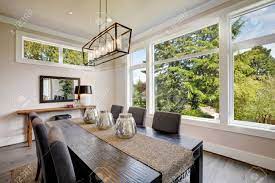 A chandelier easily becomes the centerpiece of the dining room and is the focal point for formal dining parties. Luxurious Modern Dining Room Boasts A Black Dining Table Illuminated By A Rectangular Chandelier And Surrounded By Gray Velvet Dining Chairs Over Taupe Sisal Rug Finished With Rustic Console Table Stock Photo