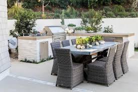 Gray Wicker Dining Chairs Surround A Dark Gray Granite Dining Table Placed In Front Of A White Brick Outdoor Kitchen Countertops Outdoor Kitchen Design Outdoor