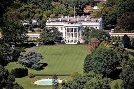 Woman in rubber gloves with hand on hip and mop looking away and smiling in american house exterior with white wooden fence. Trump To Return To White House Where Covid 19 Continues To Spread Cidrap