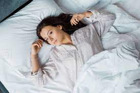 Cute woman waking up with an alarm clock. Top View Of Beautiful Girl In Pajamas Waking Up In Bed In The Morning Stock Photo Dissolve