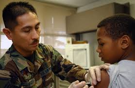 U.S. Air Force 18th Medical Operation Squadron MASTER SGT. Carlo Padua, Non  Commissioned Officer in Charge of Immunization at the Pediatric Clinic,  gives a flu shot to 10 year old Dillian Speight