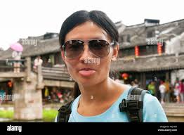 A chinese woman sticking out her tongue at the camera with Xitang water  town is blurred in the background in Jiashan county, Zhejiang province  China Stock Photo