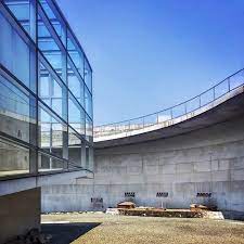ando於古墳林立的熊本設計了一座環境博物館他希望遊客於山下停車場下車後穿越樹林來到博物館入口的水 瀑牆目前已經沒放水了再經過戶外大階段拾級而上來到屋頂先俯瞰外部多處古墳再經由象徵與歷史對話的逆時鐘大斜坡時光倒流的回到過去最後鑽到博物館內部