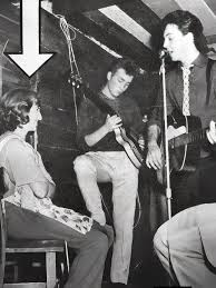 In this quietly haunting photograph, Cynthia Powell - once Cynthia Lennon - holds a framed image of her younger self sitting beside John outside Liverpool College of Art, 1959. Her hand rests
