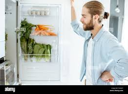 Man Choosing Products To Cook Standing Near The Refrigerator Full Of Vegetables At Home Stock Photo Alamy