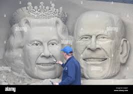 Sand sculptor "Mark Anderson" puts the finishing touches to the sculpture  of Queen Elizabeth and Prince Philip, Dorset, UK Stock Photo