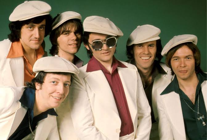 Group portrait of The Rubettes in matching 1970s light blue disco outfits and white sailor hats.