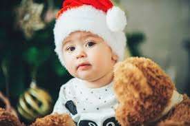 Enfant de Noël regardant la caméra et tenant un ours en peluche. Mignon  petit garçon dans un bonnet de Noel. Concept de Noël avec petit enfant,  arbre et guirlande sur fond. |