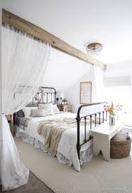 A contemporary farmhouse bedroom in neutrals, with a black metal bed, a metal sphere chandelier, a boho rug and a wreath. 49 Decorating Ideas For Farmhouse Style Bedrooms