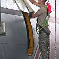 Sgt. Kyle Selman, bottom, and Cpl. Benjamin Cervantes rivet brackets into  the engine space of an F/A-18C Hornet.