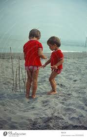Zwei kleine Mädchen im Partnerlook, spielen am Strand, bauen mit Stöcken  einen Zaun und lauschen dem Meer zu. - ein lizenzfreies Stock Foto von  Photocase