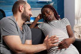 Cheerful interracial couple expecting baby at home. Caucasian husband and  pregnant african american wife touching baby bump together smiling. Multi  ethnic people with pregnancy. Stock Photo | Adobe Stock