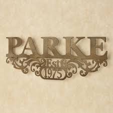 Aged iron squares featuring a ribbed concave center in antique gold, washed with a heavy patina glaze revealing ivory undertones. Kinship Antique Gold Family Name And Year Personalized Metal Wall Art Sign