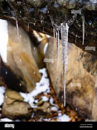 Detail Close Shot of Large Icicle with smaller icicles hanging off a rock  formation with warm-colored rocks and snow in the background Stock Photo -  Alamy