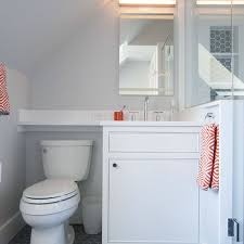 Elegant attic bathroom features sloped ceiling fitted with skylight above a roll top pedestal tub with floor mount gooseneck tub filler and hand shower framed by gray walls boasting a heated towel rack across from a purple accent chair studded with a band of square silver nailhead trim atop gray and. Attic Bathroom Sloped Ceiling Design Ideas