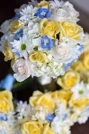 Happy bride in elegant wedding dress holding flowers while sitting in armchair and touching face on white. Blue Yellow And White Bouquets