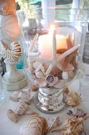 A covered beach patio with white and light blue furniture, blue printed pillows and a unique centerpiece of. Beach Inspired Wedding