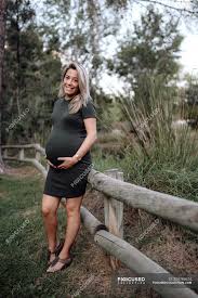 Maybe you would like to learn more about one of these? Beautiful Pregnant Woman In Casual Dress Smiling And Holding Hands On Belly While Standing Next To Wooden Bridge Green Summer Stock Photo 324788624