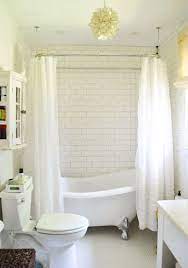 Large bright white traditional bathroom features a white catty corner vintage silver clawfoot bathtub with a vintage handheld tub filler under windows, flanked by white quartz topped washstands that boast vintage hook spout. House Crashing Breezy Bright Young House Love Bathroom Inspiration Clawfoot Tub Shower Bathroom Design