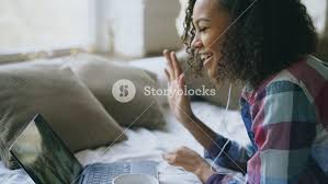Curly african american young woman having video chat with friends using  laptop camera while lying on bed Royalty-Free Stock Image - Storyblocks