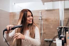 Beautiful Young Smiling Woman Using A Hair Straightener While Looking Into  The Mirror In Bathroom Stock Photo - Download Image Now - iStock